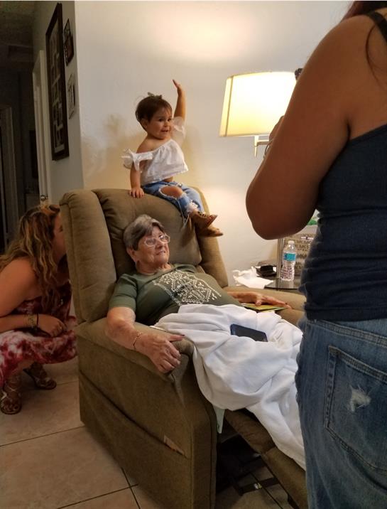 A toddler joyfully plays on a chair while relatives interact in a warm living room setting.