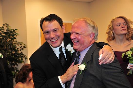 Two men share a warm laugh while celebrating together, surrounded by joyful guests.