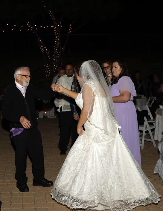 Guests are dancing joyfully at a wedding reception amidst lights and decorations.