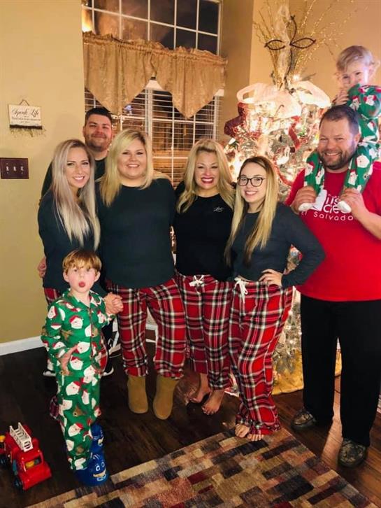 A happy family poses in matching pajamas by a beautifully decorated Christmas tree.