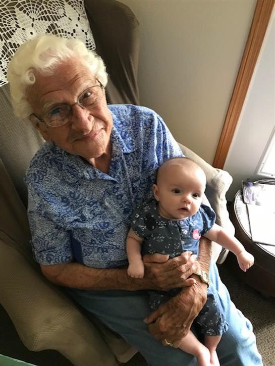 A lovely great-grandparent holds a baby in a comfortable chair, radiating warmth and love.