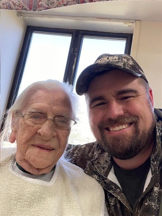 A young man shares a joyful moment with an elderly woman, both smiling warmly in a sunlit room.