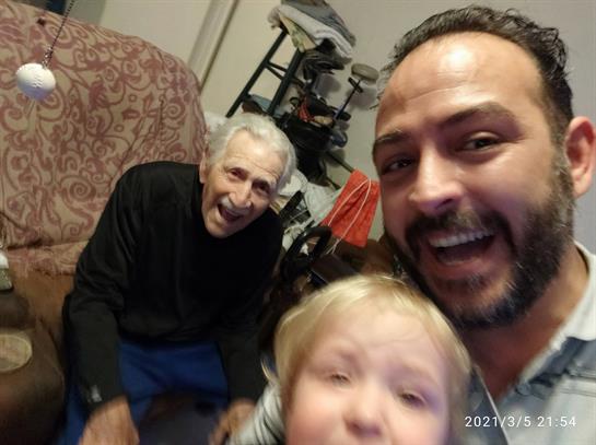 Adult man enjoys a playful moment with an elderly person and a child in a warm living space.