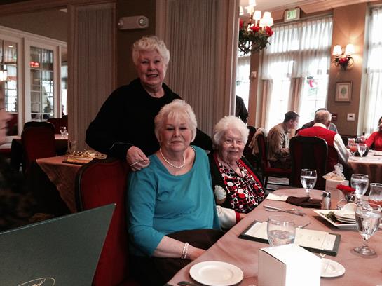 Three older women share smiles and laughter at a restaurant while celebrating the holidays.
