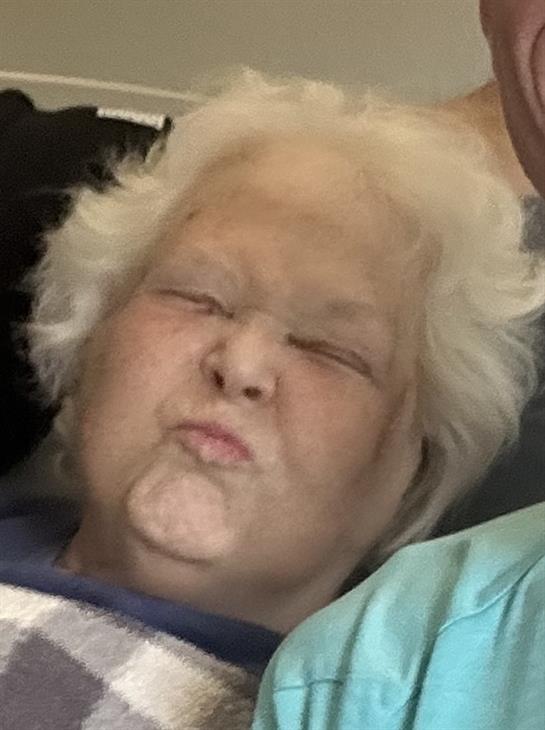 A lively elderly woman is playfully making a funny face while surrounded by family members.