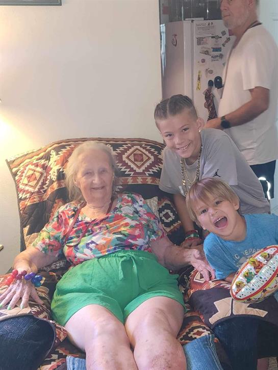 A grandmother, her grandchild, and a family member share smiles and laughter in a living space.