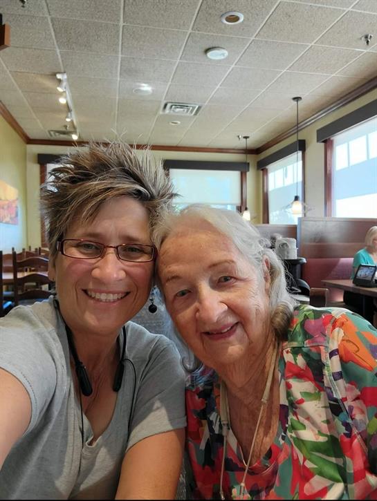 Two women smile warmly as they take a selfie, seated together in a lively restaurant.