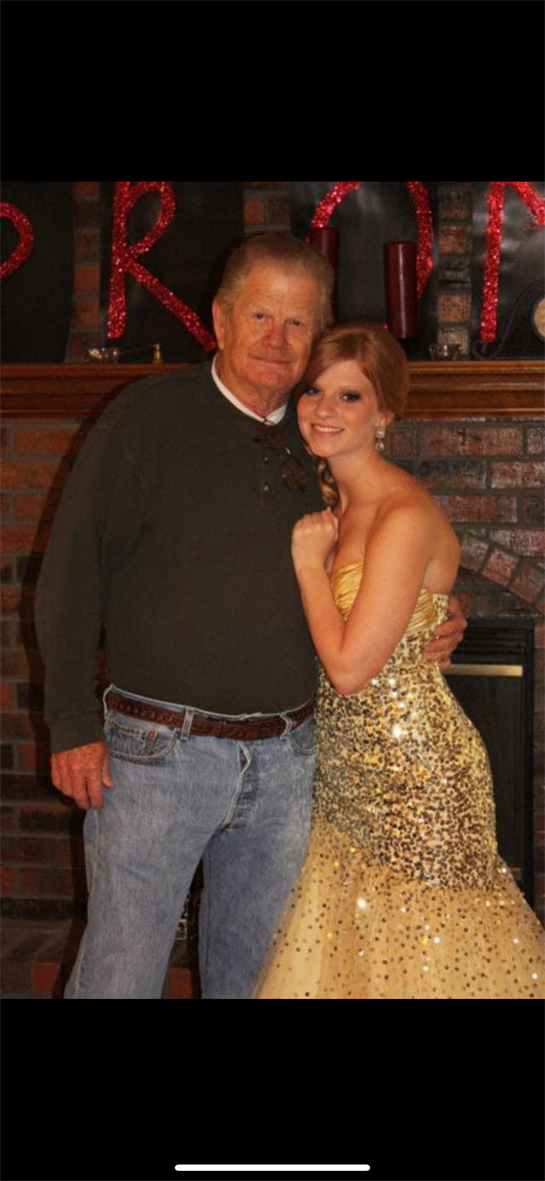 A young woman in a glittering gown poses happily with an older man, showcasing their bond.