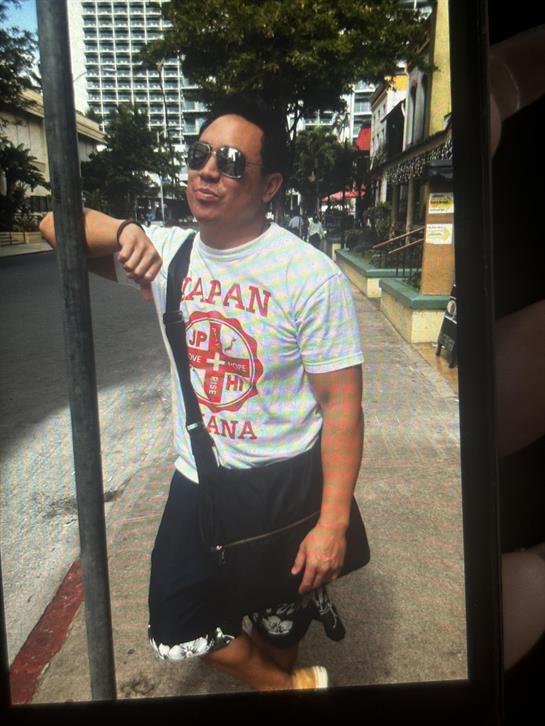 A man in sunglasses and a graphic tee relaxes on a sunny city street.