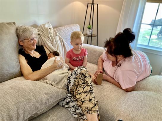 Three generations share joyful moments, a newborn in a blanket, laughter all around.