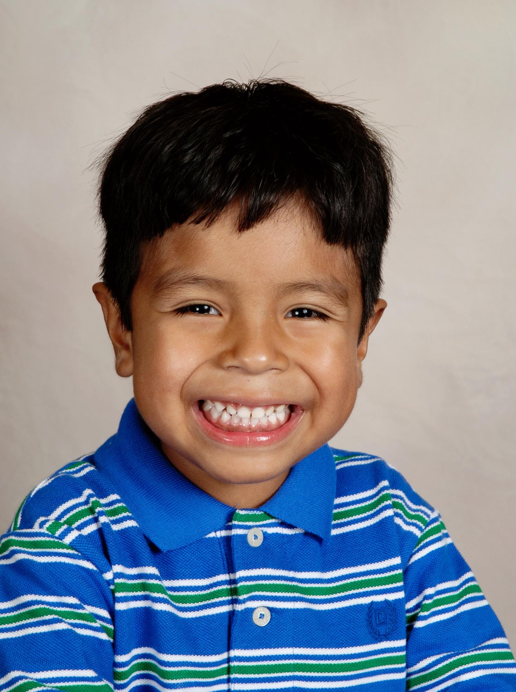 Boy with short black hair smiles widely, exuding joy and a bright personality.