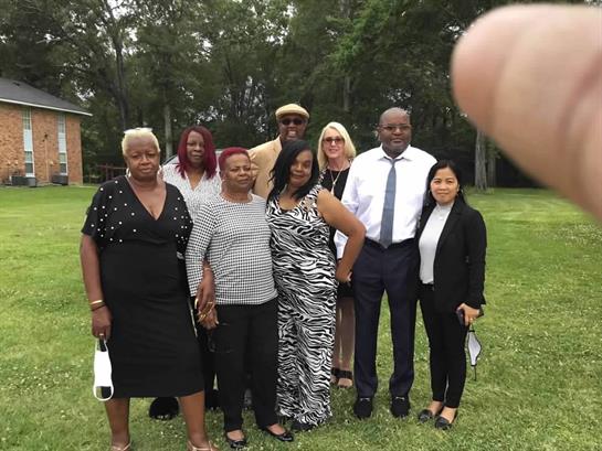 A diverse family gathering takes place in a lush green yard with smiles and casual attire.