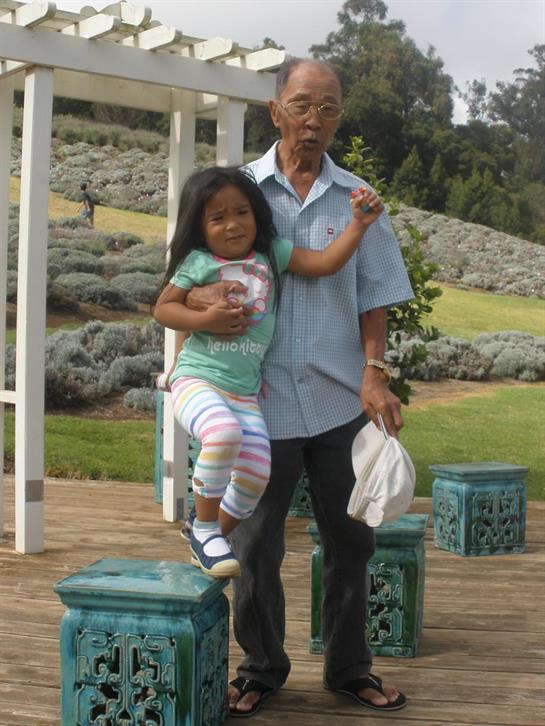 A cheerful grandfather interacts playfully with his granddaughter in a lush garden setting.