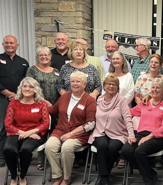 A large group of individuals poses together, smiling, at a reunion event held indoors.