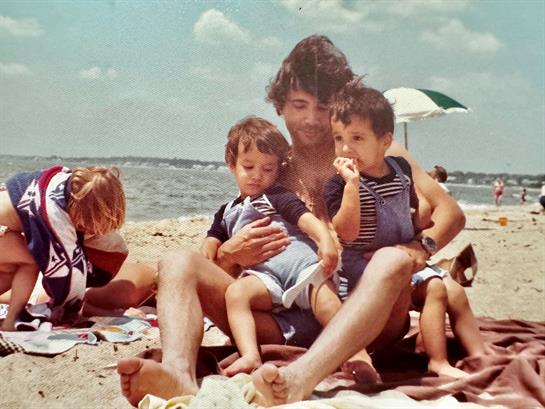 A father enjoys the sun with his kids on a blanket at the beach.