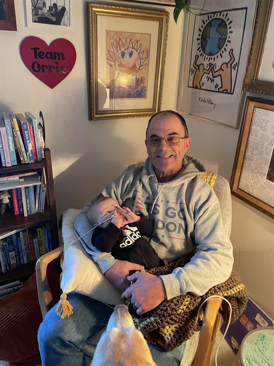 An elderly man cherishes a quiet moment with a baby in a cozy room of books and art.