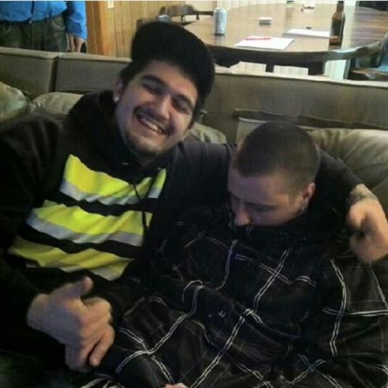 Two friends smile and lounge on a couch in a casual indoor gathering, sharing a comfortable moment.