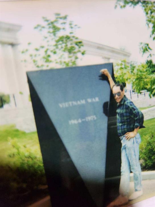 Person stands beside a black granite Vietnam War memorial in a grassy area.