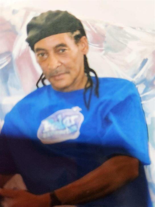 Portrait of a man with long braided hair wearing a blue shirt, appearing relaxed and focused.