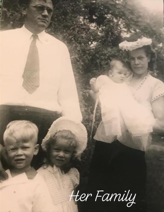 A loving family stands together in a sunny garden, dressed in vintage clothing, smiling joyfully.