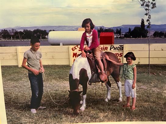 Three young children interact with a pony at a fair, creating joyful memories in the sun.