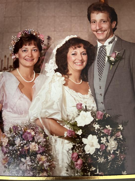 Two bridesmaids and a groom stand together, smiling with floral arrangements in their hands.
