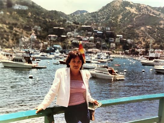 A woman stands by the harbor, smiling and enjoying the beautiful sunny weather surrounded by boats.