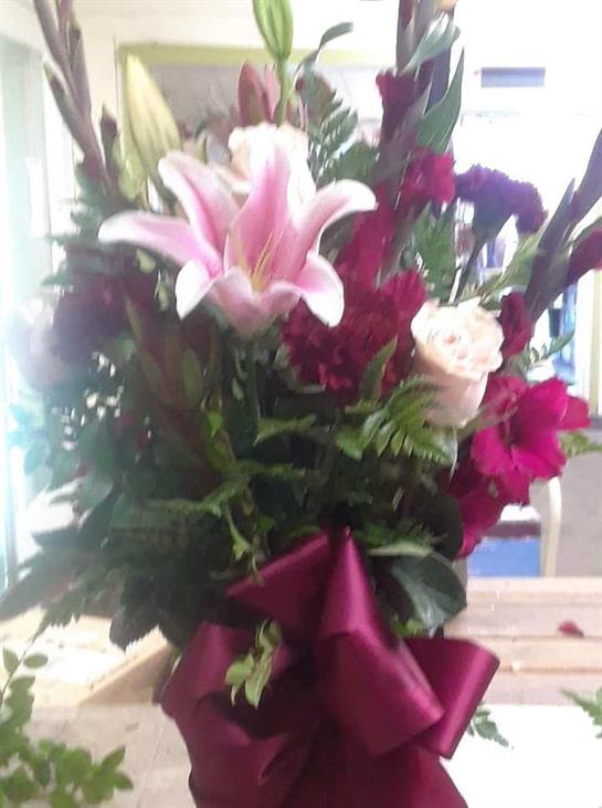 A vibrant bouquet showcases pink lilies, red flowers, and white roses, neatly tied with a ribbon.