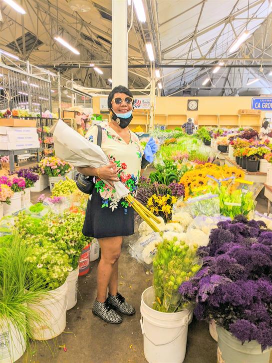 A vendor delights in choosing colorful flowers amidst a lively market filled with greenery.