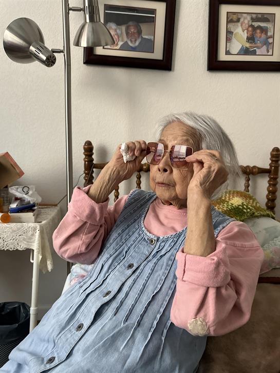 An elderly woman adjusts her glasses, enjoying the cozy warmth of her home.