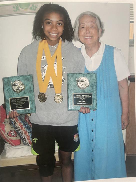 Young woman shows her athletic achievements with medals and trophies next to a smiling elder.