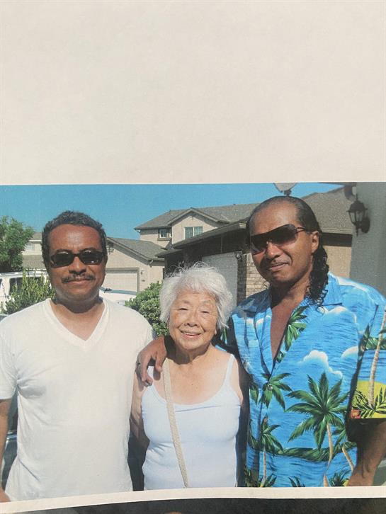 Three relatives gather outdoors, smiling and sharing a joyful moment in a vibrant neighborhood.