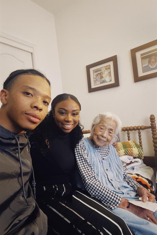 Three family members share smiles and laughter in a comfortable living room setting.