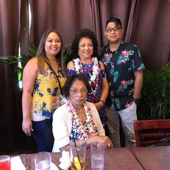 A group of four people smiles together while wearing floral leis at a restaurant table.