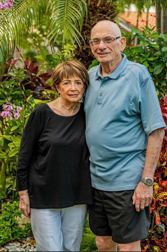 A couple poses lovingly in a beautiful garden filled with colorful plants and flowers.