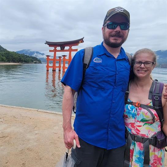 A man and woman standing on a beach with a red torii gate