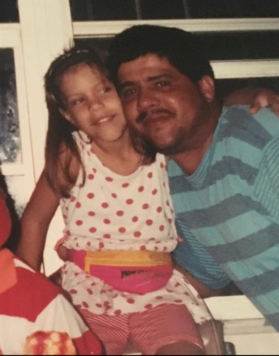 A joyful child sits on a man's lap, both sharing a warm smile in a casual indoor space.