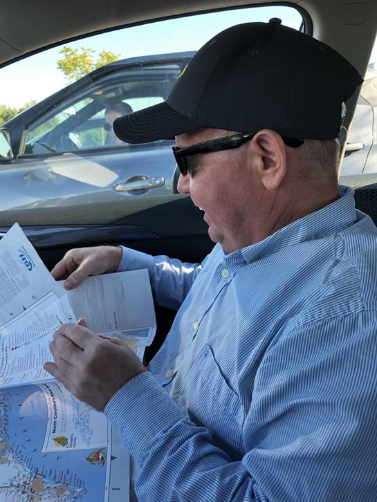 Man is intently looking at a map while seated in a parked car. Sunlight filters in.