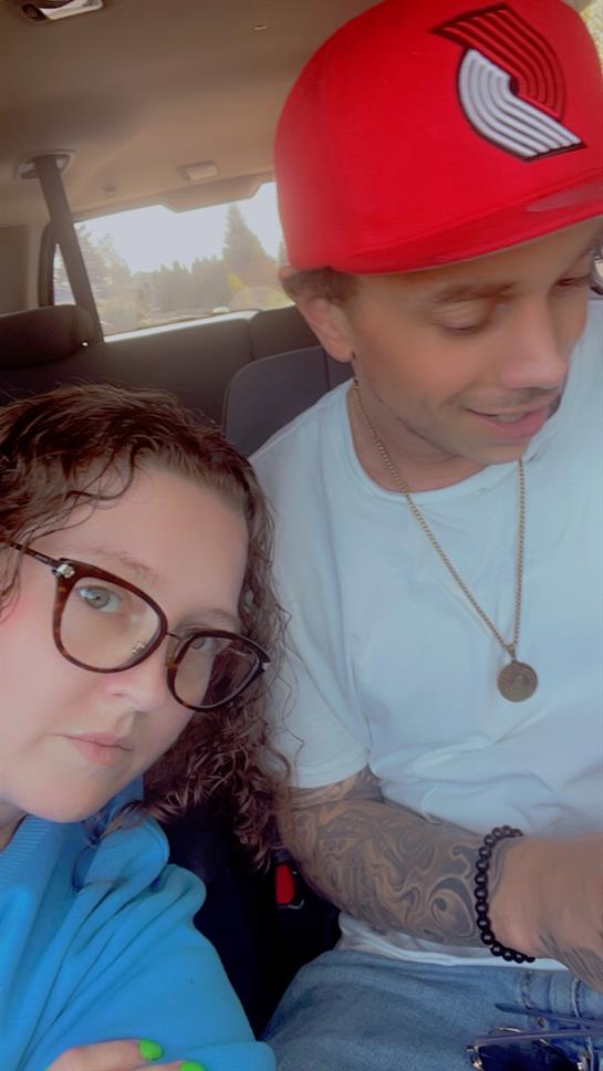 Two friends share a moment in a car, smiling and engaged with their phones while enjoying the day.