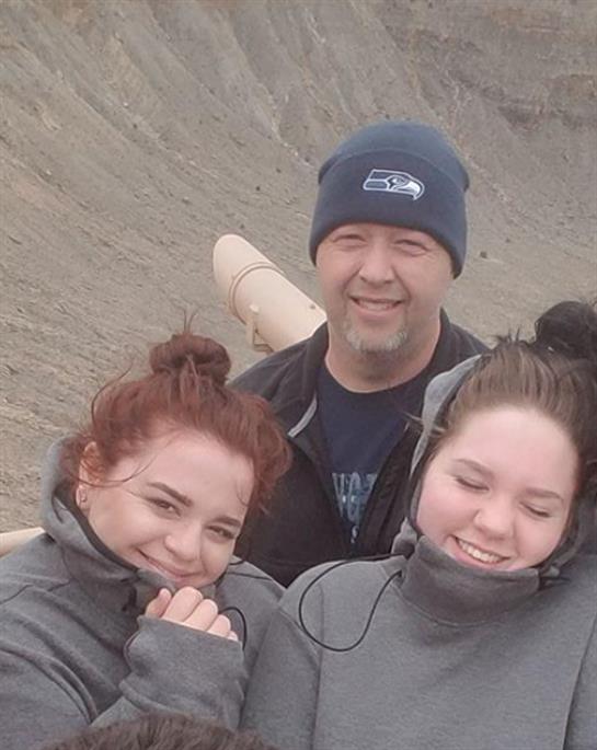 Three people enjoy a windy day outdoors while smiling and standing close together in warm clothing.