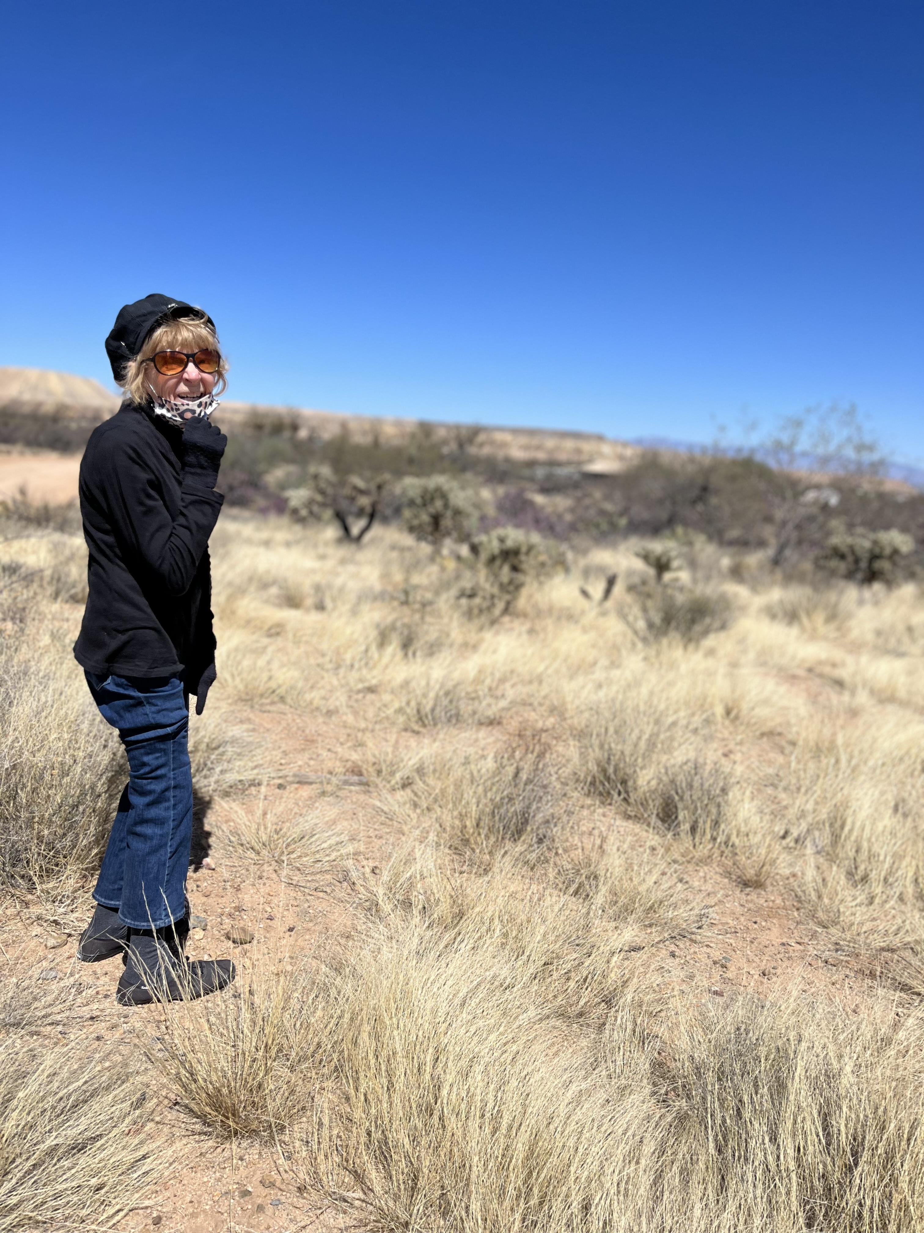 Young child stands alone in a vast desert, surrounded by tall grass and sparse vegetation.