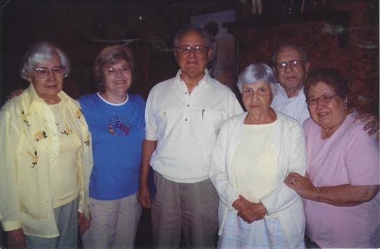 Six family members gathered indoors, smiling and enjoying a moment together while sharing stories.