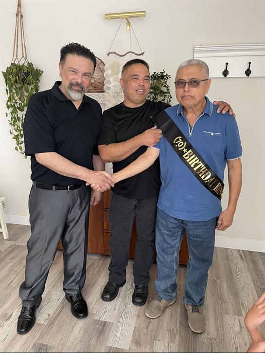 Three men celebrate a milestone birthday, exchanging greetings and enjoying the moment together.