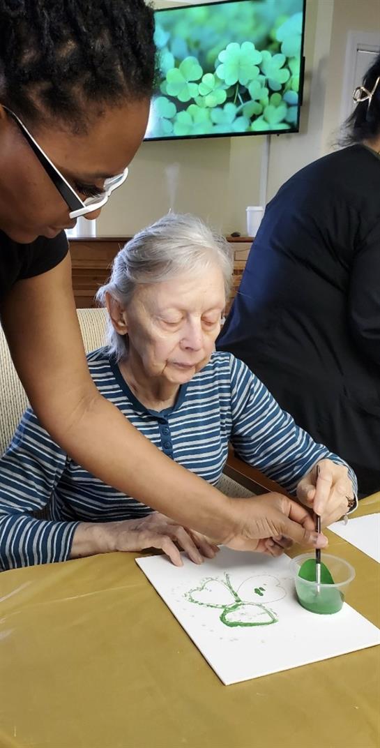A woman painting a piece of paper with a woman in the background
