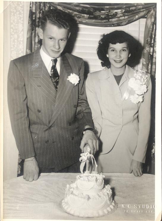 Newlywed couple smiling while cutting a wedding cake in a charming vintage room.