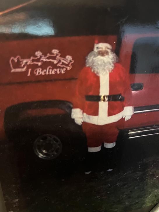 Santa Claus greets holiday visitors beside a cheerful red truck featuring decorations.