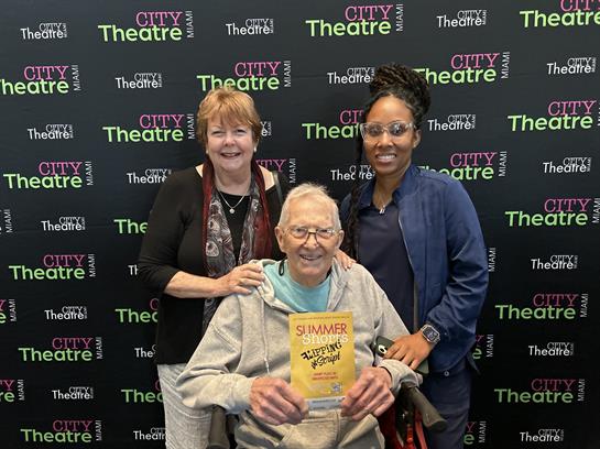 Three individuals pose together at City Theatre, sharing smiles and holding a program.