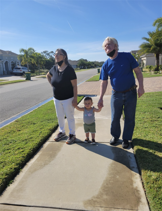 A child holds hands with grandparents while walking down a sunny suburban sidewalk.