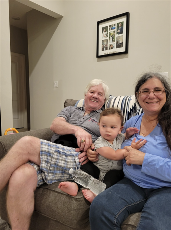 An elderly couple enjoys quality time with a toddler, sharing smiles in a comfy living room.