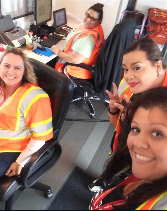 Four workers in safety vests are enjoying a break and taking a selfie at their workspace.